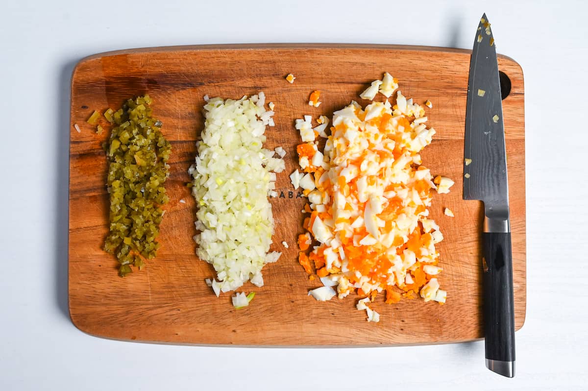 Finely diced pickled gherkin, onion and boiled egg on a wooden chopping board