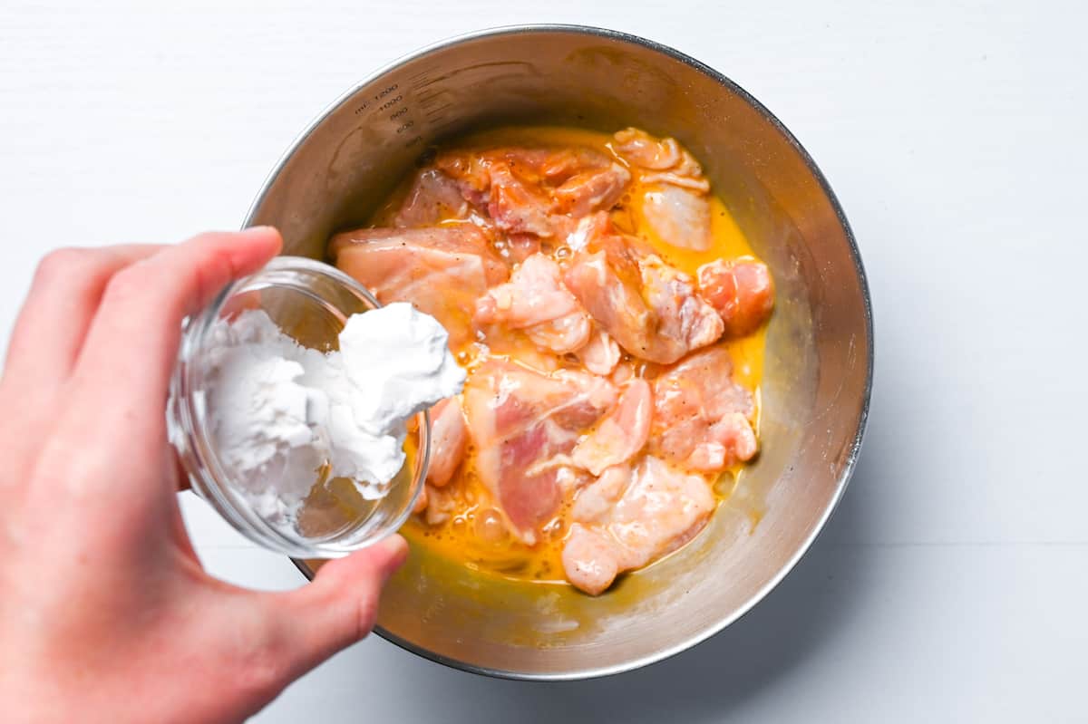 Adding potato starch to chicken and egg in a steel mixing bowl