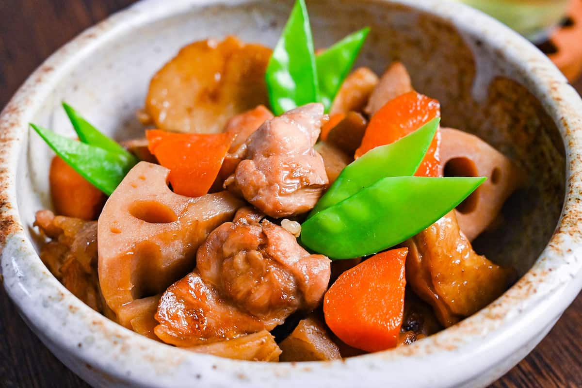 Chikuzenni (Japanese simmered chicken and vegetables) served in a mottled beige bowl side view close up