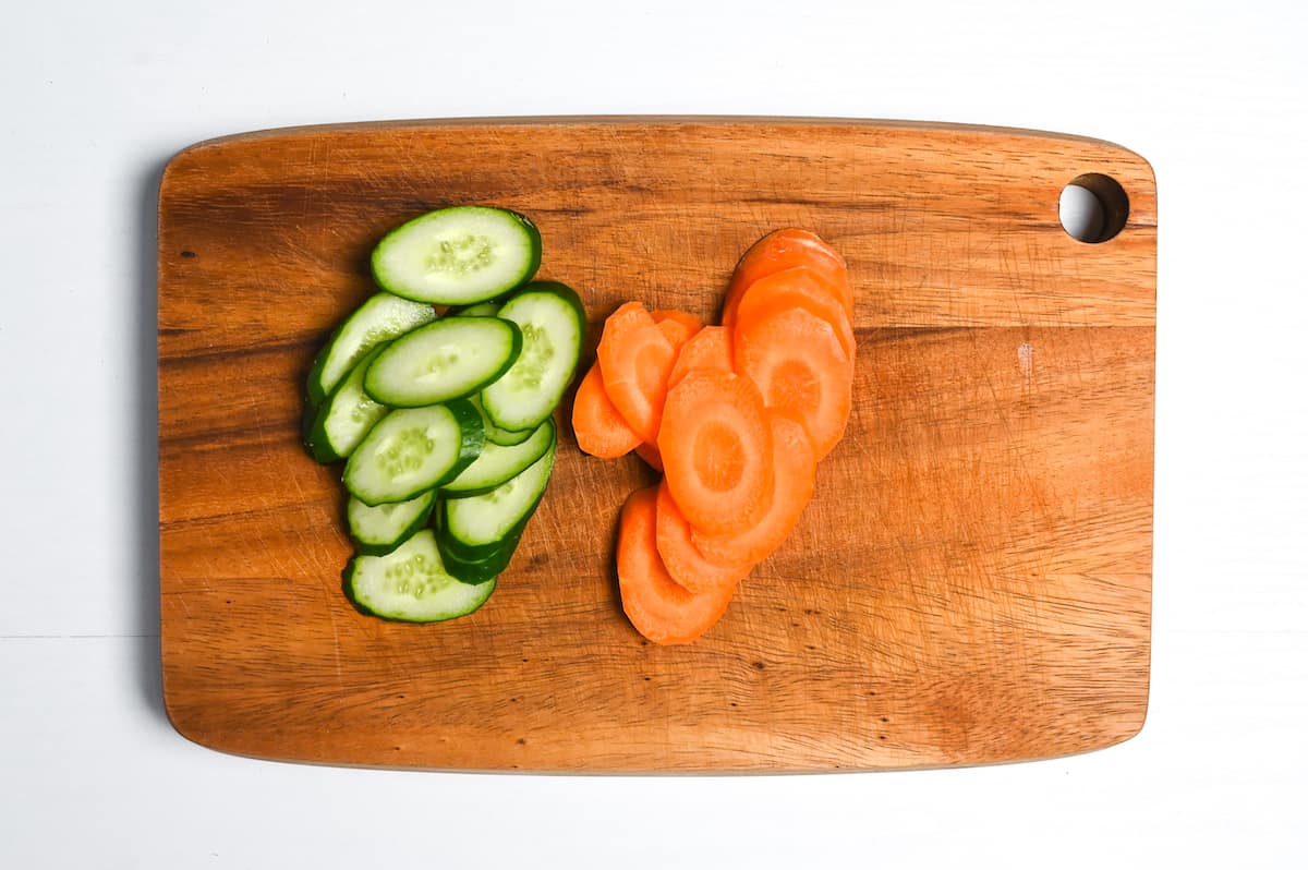 Carrot and cucumber diagonally sliced on a wooden chopping board