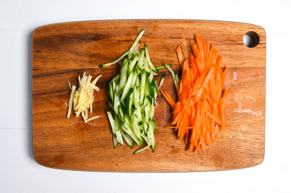 Julienned fresh ginger, cucumber and carrot on a wooden chopping board