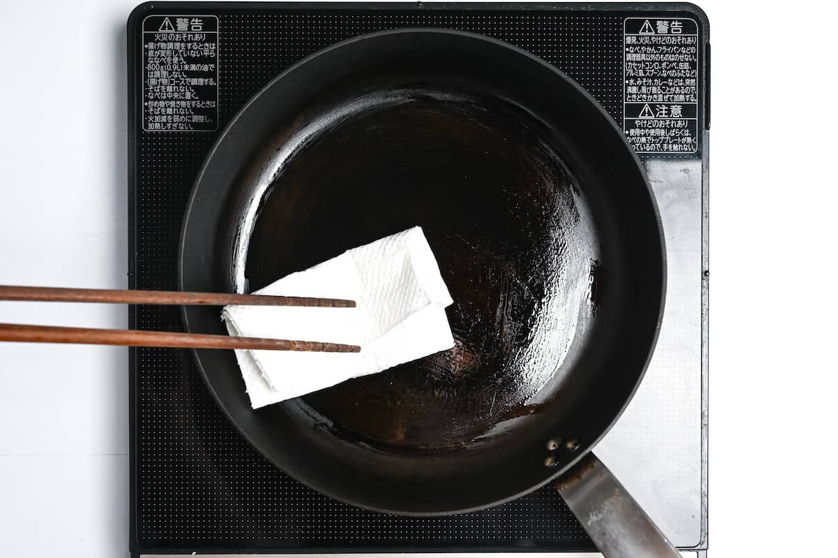wiping excess oil in a pan with a piece of kitchen paper