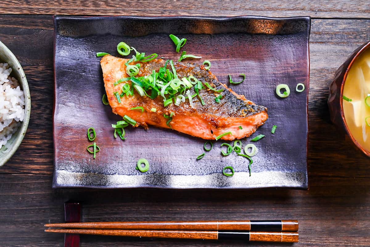 Miso glazed salmon (pan fried) served on a brown rectangular plate and sprinkled with spring onions