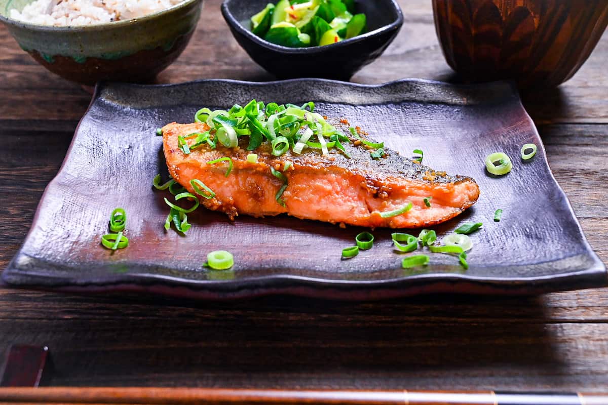 Miso glazed salmon (pan fried) served on a brown rectangular plate and sprinkled with spring onions