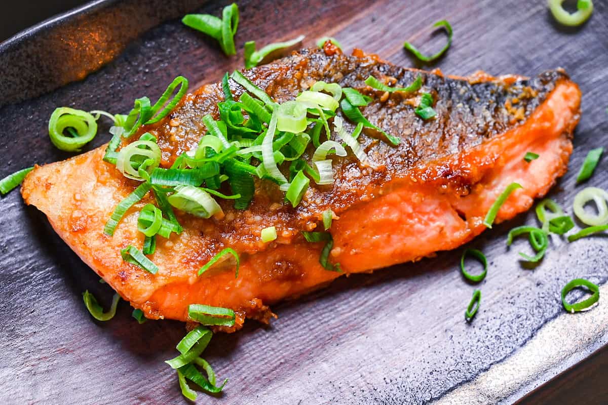 Miso glazed salmon (pan fried) served on a brown rectangular plate and sprinkled with spring onions