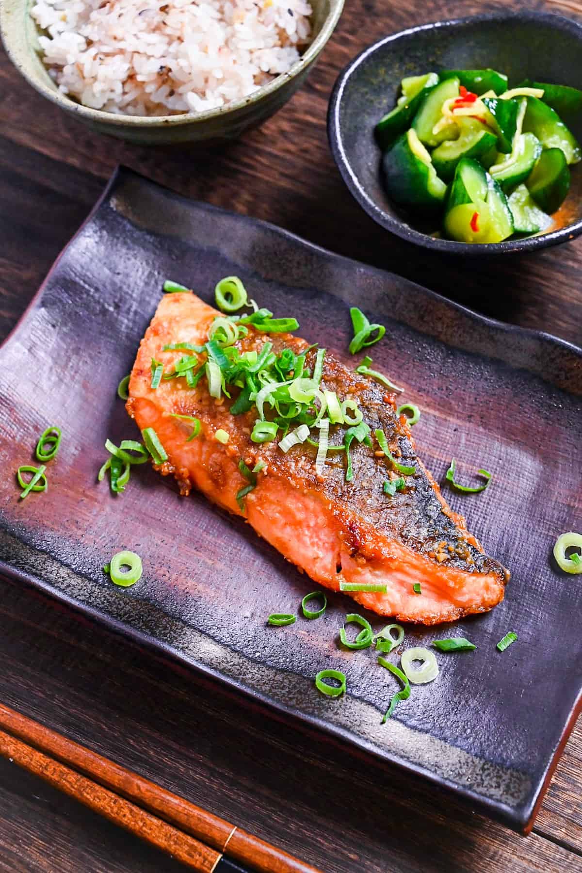 Miso glazed salmon (pan fried) served on a brown rectangular plate and sprinkled with spring onions