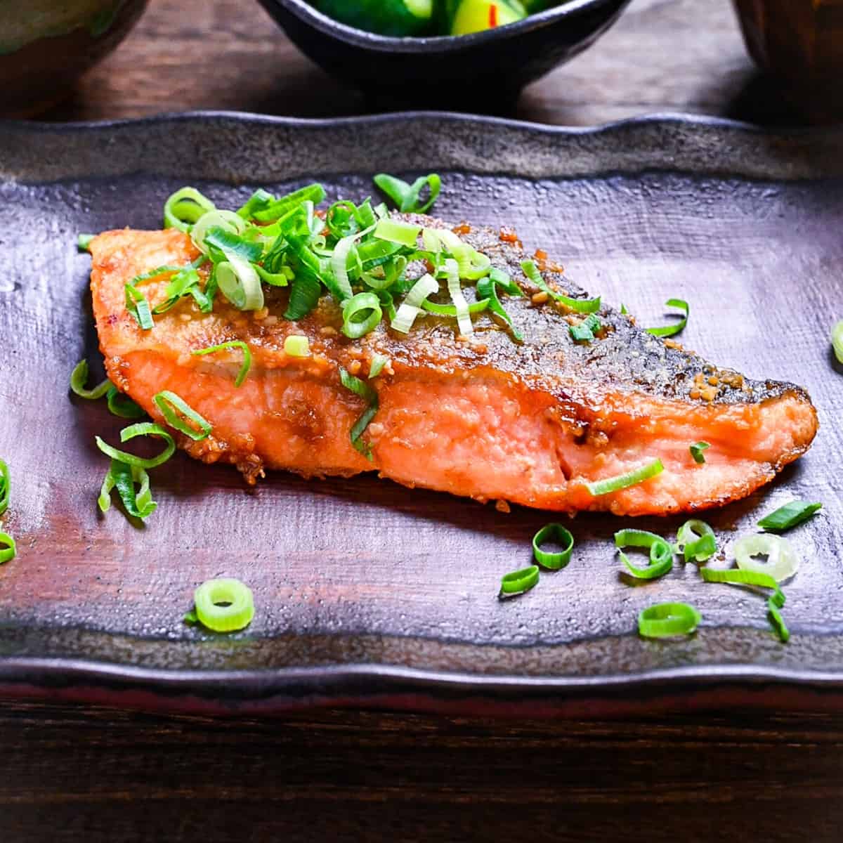 Miso glazed salmon (pan fried) served on a brown rectangular plate and sprinkled with spring onions
