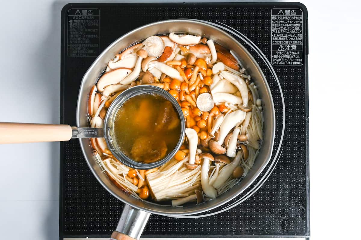 miso paste in a mesh spoon placed in pot of mushrooms and dashi