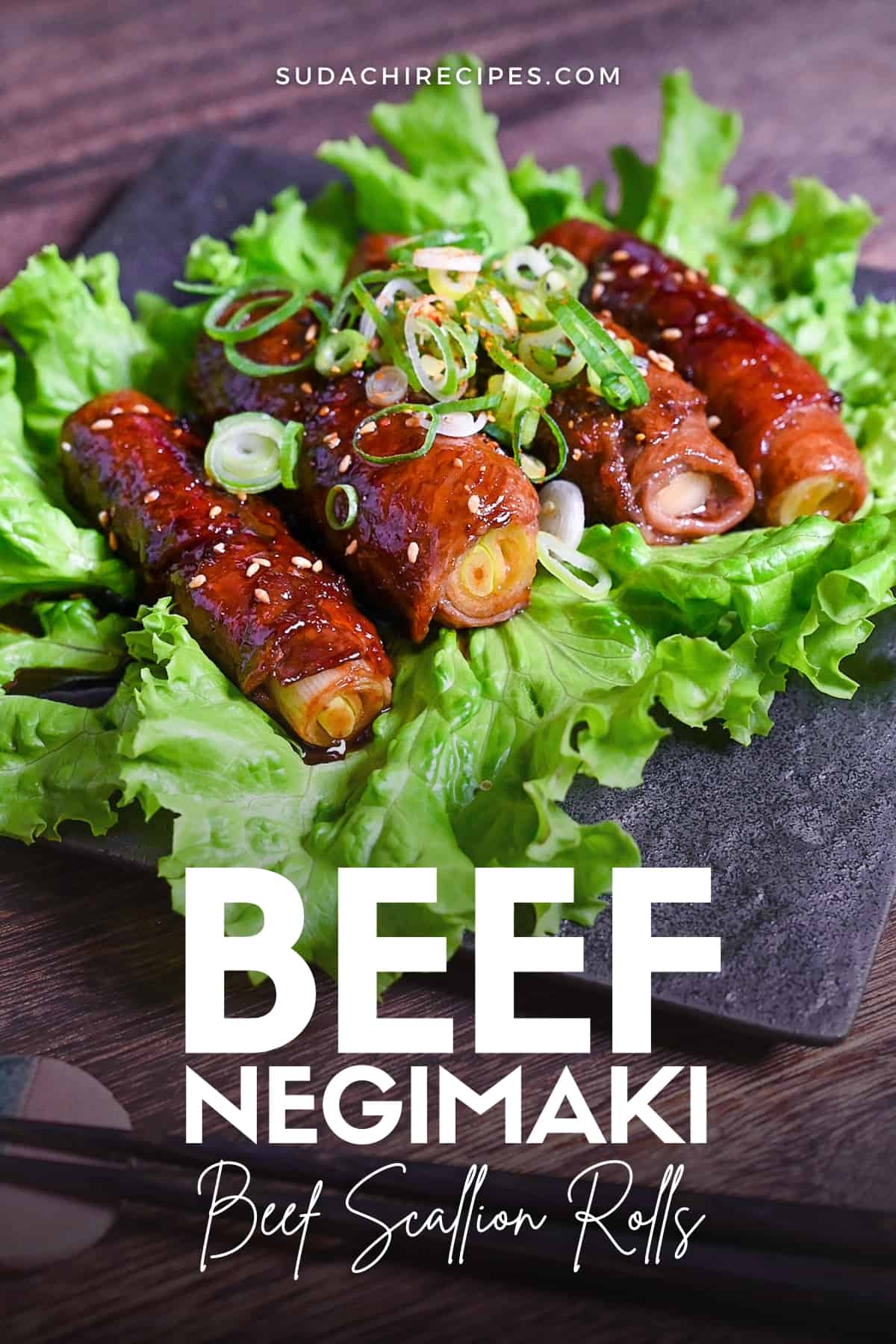 Beef Negimaki (Japanese Beef Scallion Rolls) served on a square black plate upon a bed of lettuce and sprinkled with sesame seeds
