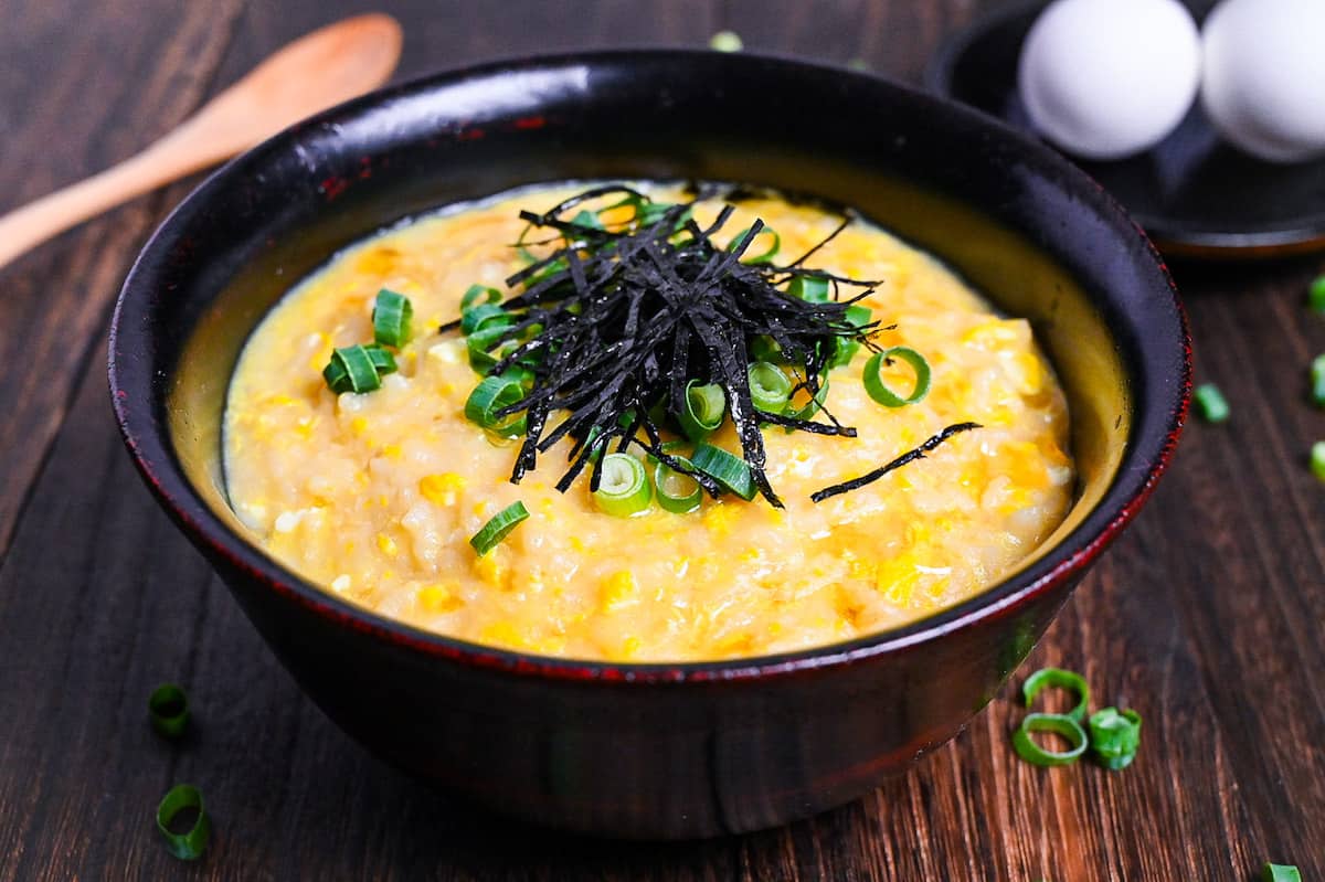 Okayu (Japanese Rice Porridge) with egg in a black lacquerware bowl sprinkled with spring onion and kizami nori