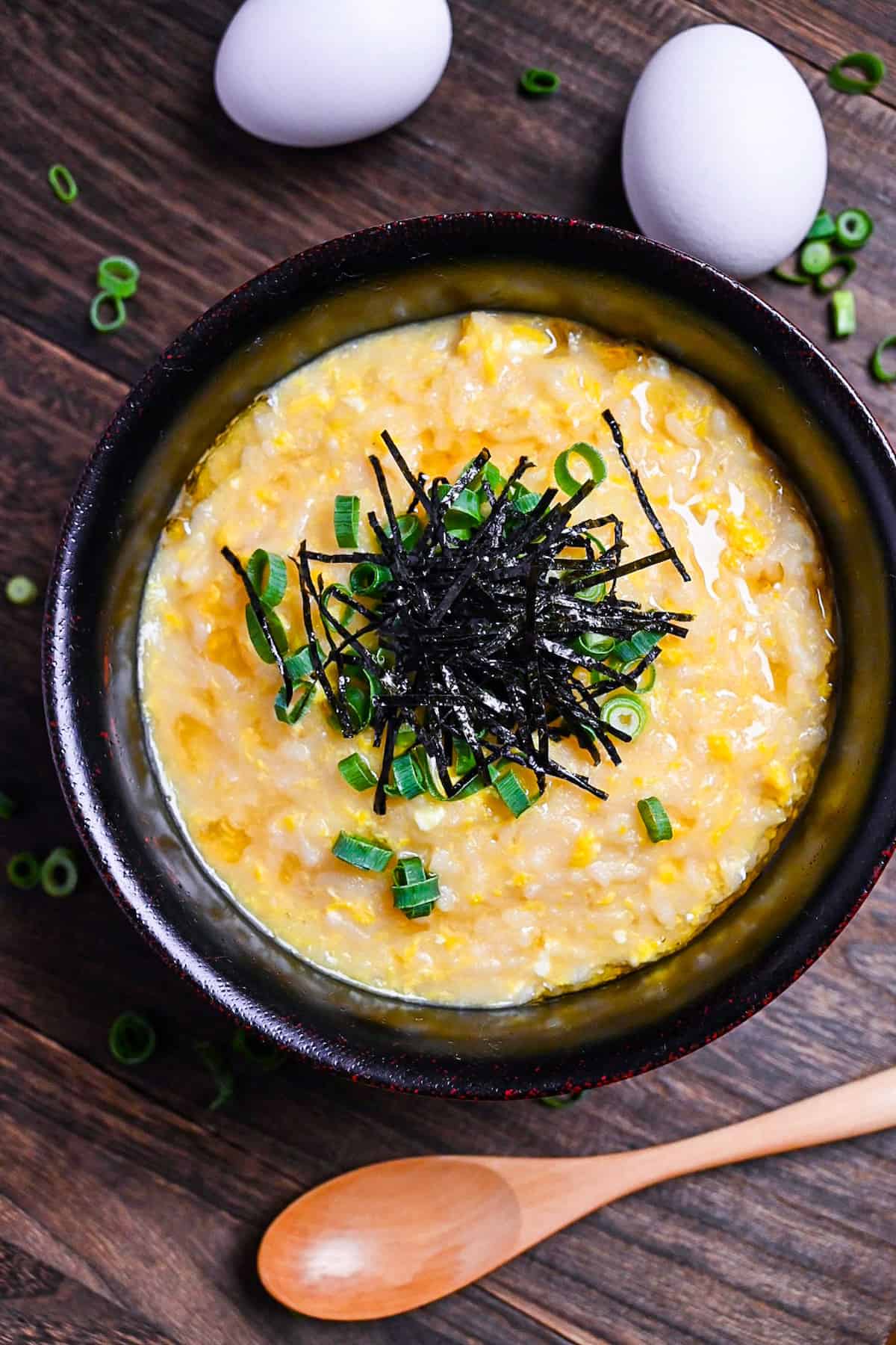 Okayu (Japanese Rice Porridge) with egg in a black lacquerware bowl sprinkled with spring onion and kizami nori