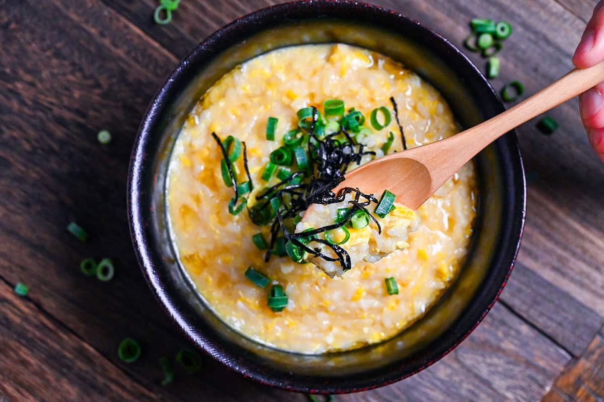 Okayu (Japanese Rice Porridge) with egg in a black lacquerware bowl sprinkled with spring onion and kizami nori