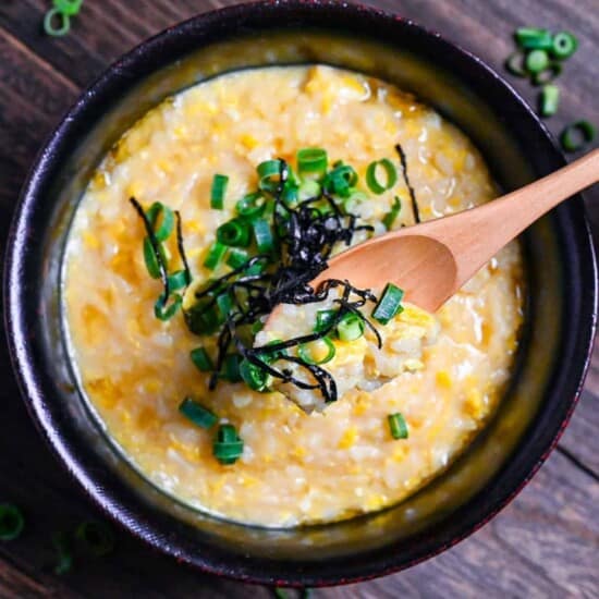 Okayu (Japanese Rice Porridge) with egg in a black lacquerware bowl sprinkled with spring onion and kizami nori