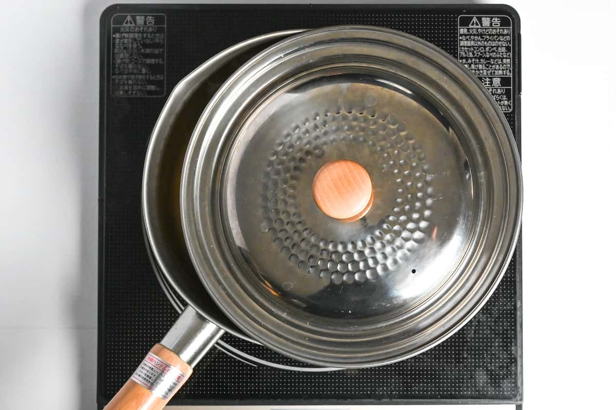 Simmering okayu in a pot with a lid placed slightly ajar