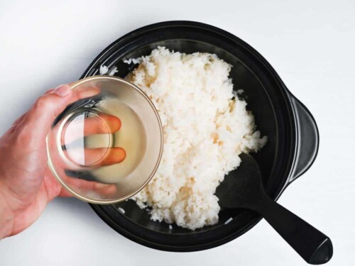 adding sushi vinegar to cooked rice in a pot