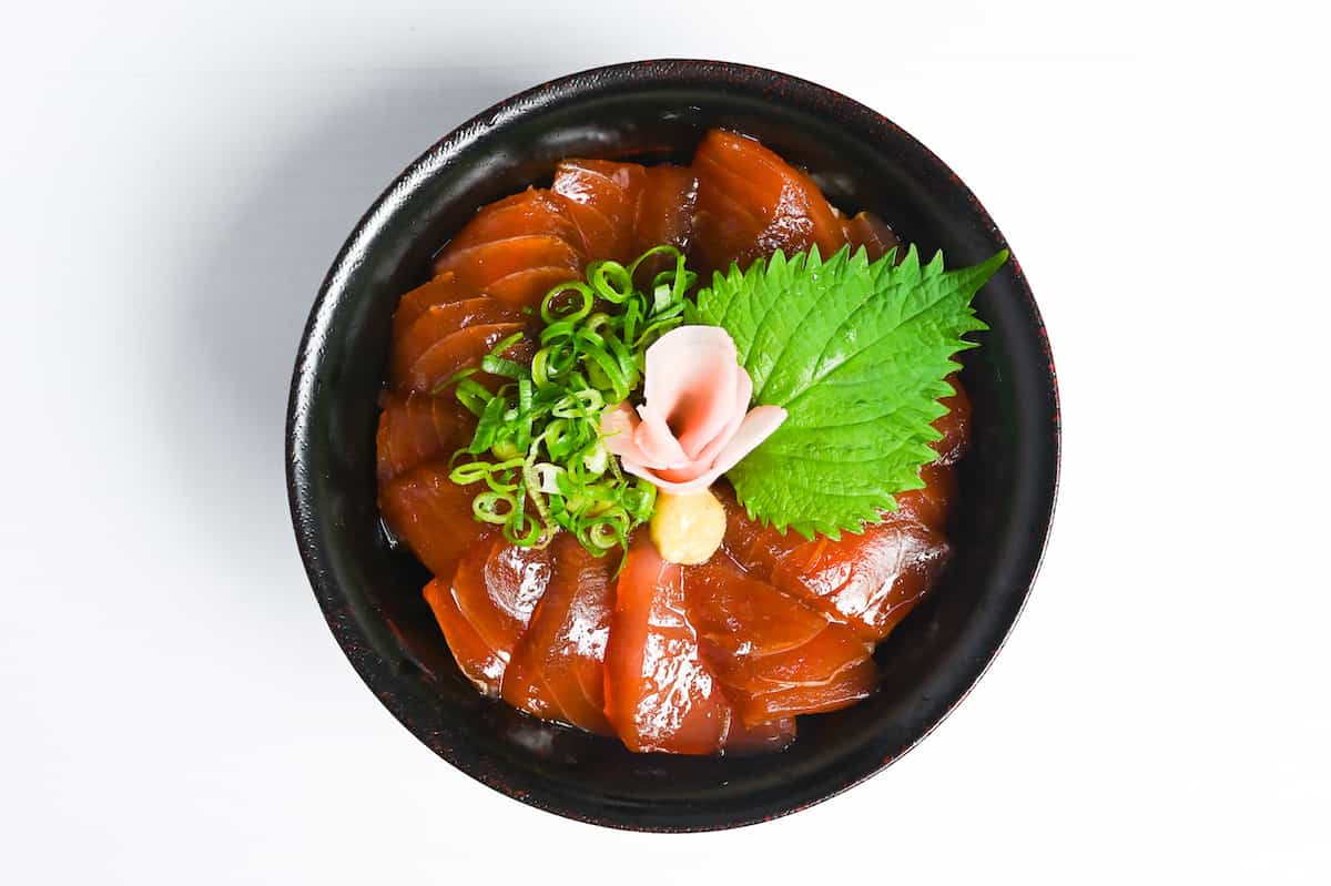 Tekkadon in a black lacquerware bowl topped with ooba leaf, gari (pickled ginger), wasabi and chopped spring onion