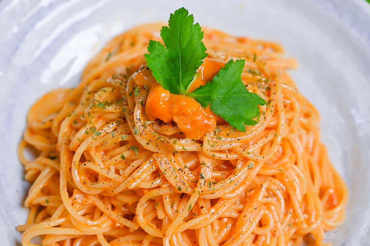 Japanese uni cream pasta served on a white plate and topped with black pepper and parsley close up