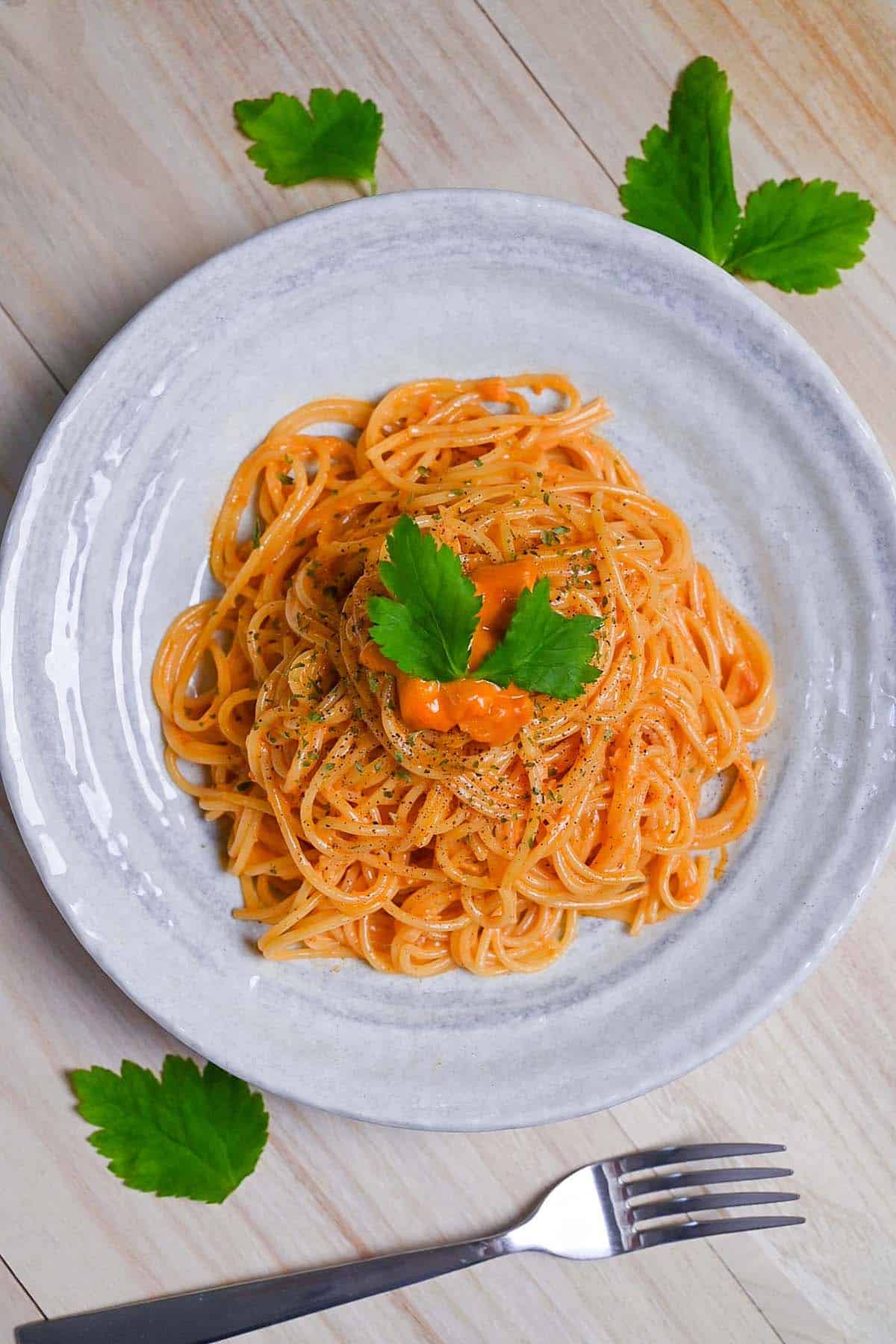 Japanese uni cream pasta served on a white plate and topped with black pepper and parsley top down vertical