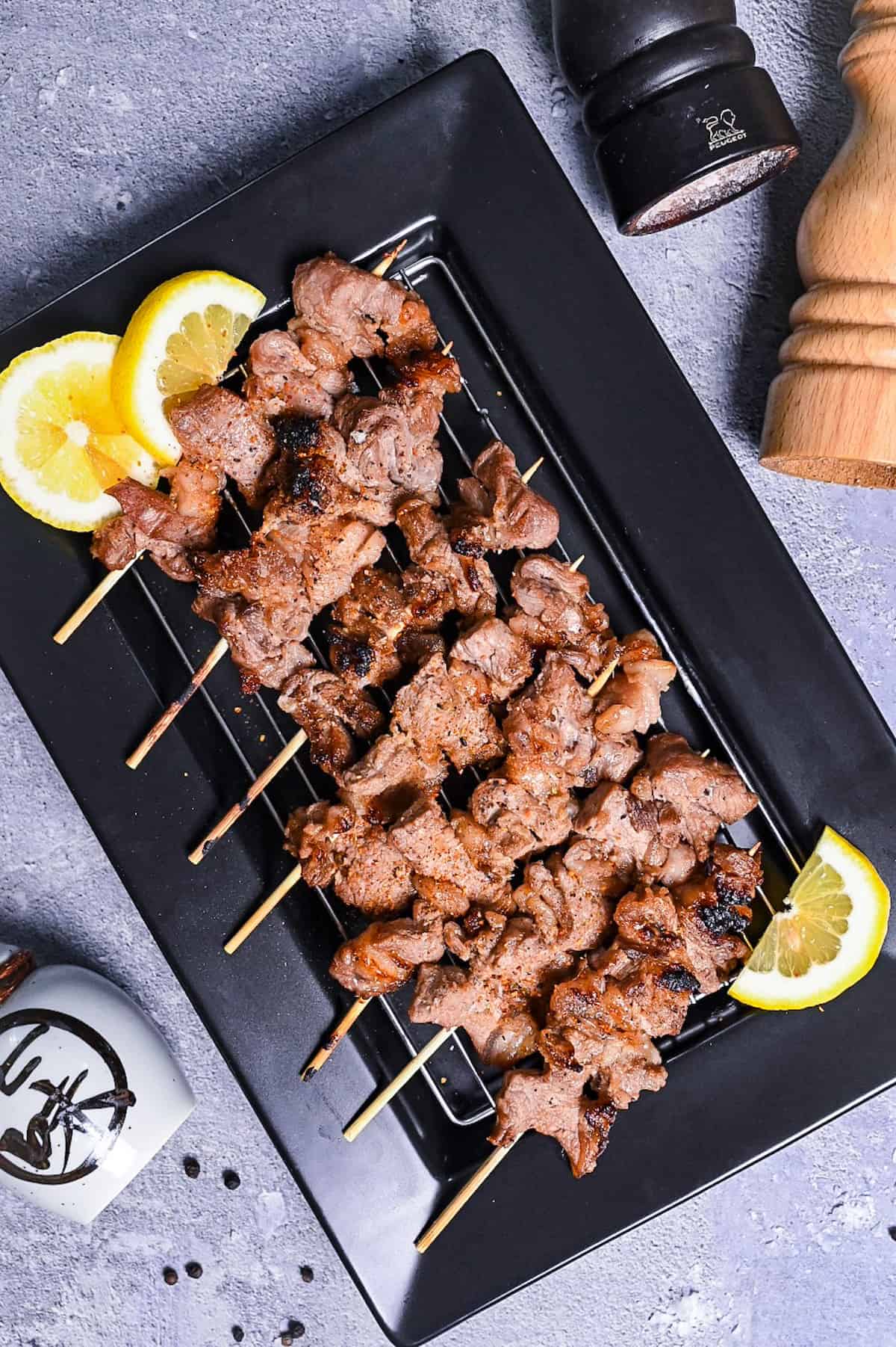 Beef Kushiyaki (Japanese Beef Skewers) served on a black rectangular plate with lemon wedges