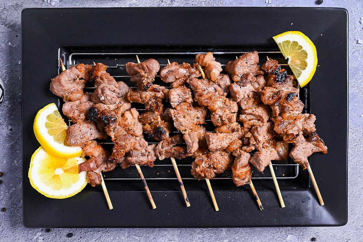 Beef Kushiyaki (Japanese Beef Skewers) served on a black rectangular plate with lemon wedges