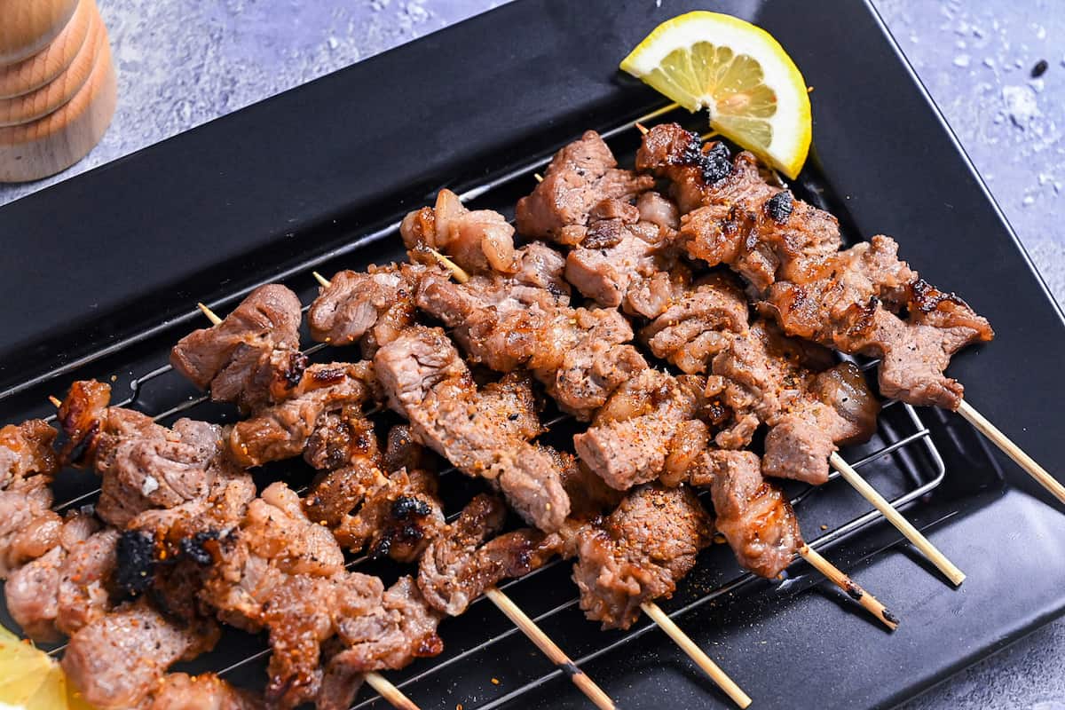 Beef Kushiyaki (Japanese Beef Skewers) served on a black rectangular plate with lemon wedges