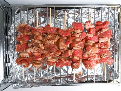 Marinated beef pushed onto skewers and placed on a wire rack ready for grilling