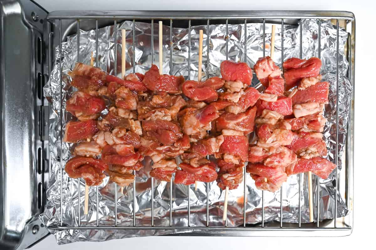 Marinated beef pushed onto skewers and placed on a wire rack ready for grilling