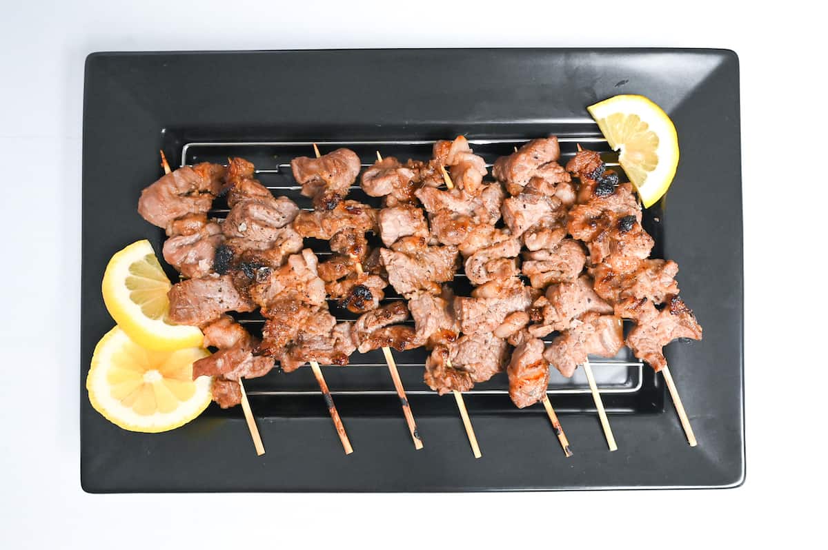 Beef Kushiyaki (Japanese Beef Skewers) on a black rectangular plate with lemon wedges