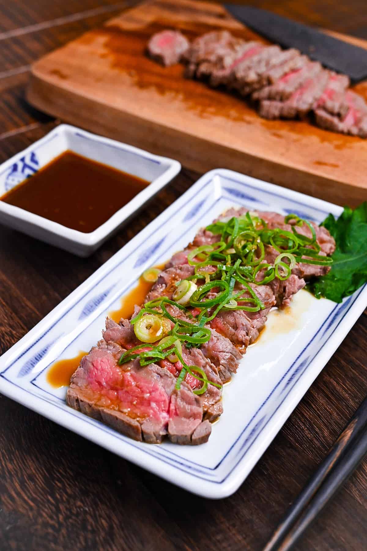 Beef tataki (Japanese seared beef fillet) on a white plate topped with homemade sauce and chopped green onions