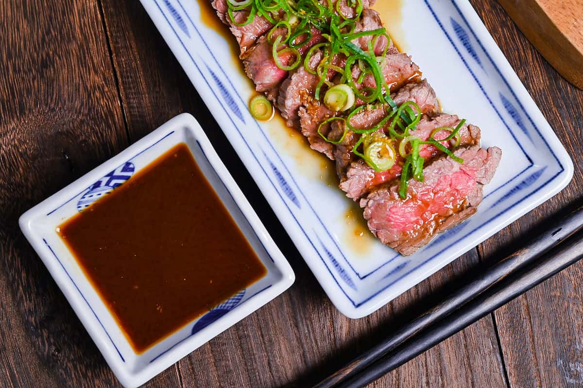 Beef tataki (Japanese seared beef fillet) on a white plate topped with homemade sauce and chopped green onions