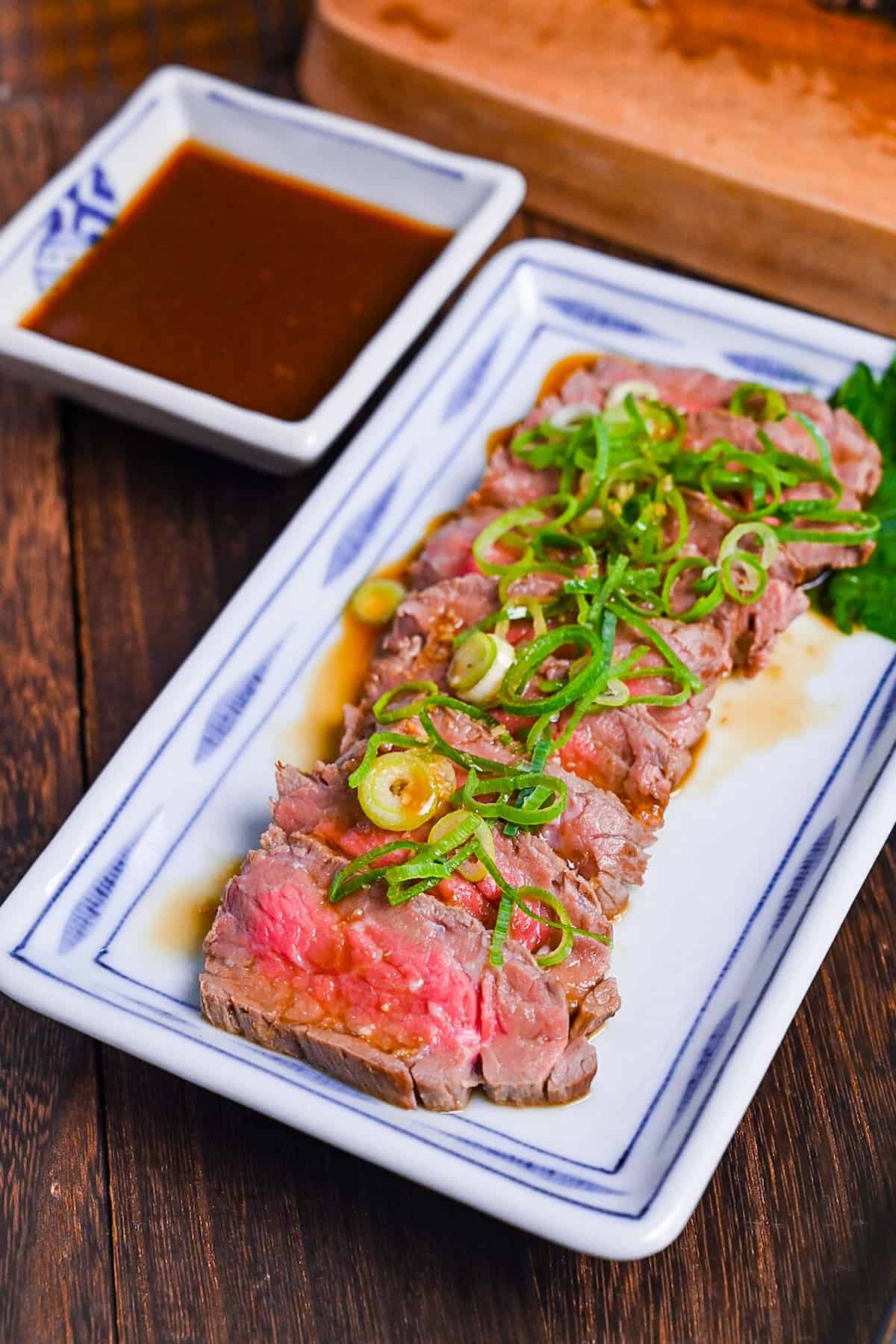 Beef tataki (Japanese seared beef fillet) on a white plate topped with homemade sauce and chopped green onions