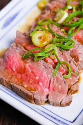 Beef tataki (Japanese seared beef fillet) on a white plate topped with homemade sauce and chopped green onions