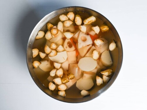 Cut burdock root, lotus root, taro and carrot soaking in a bowl of water