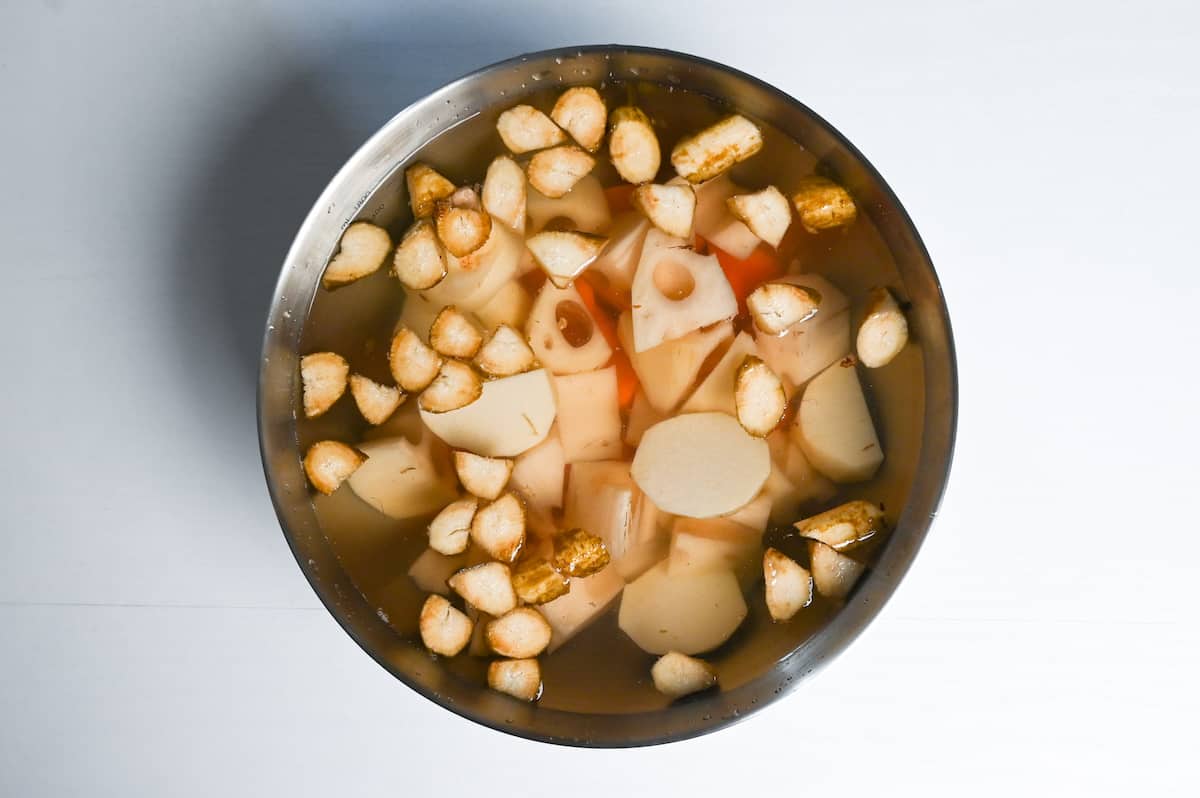 Cut burdock root, lotus root, taro and carrot soaking in a bowl of water