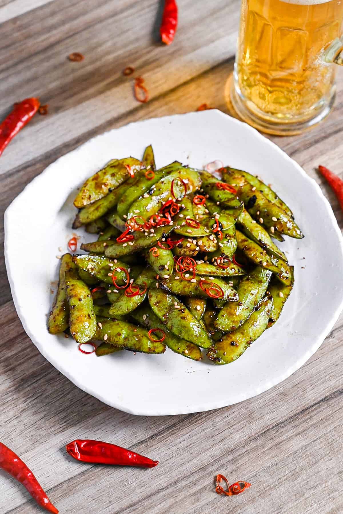 Stir fried edamame with garlic and oyster sauce glaze topped with dried chili and sesame seeds on a white plate