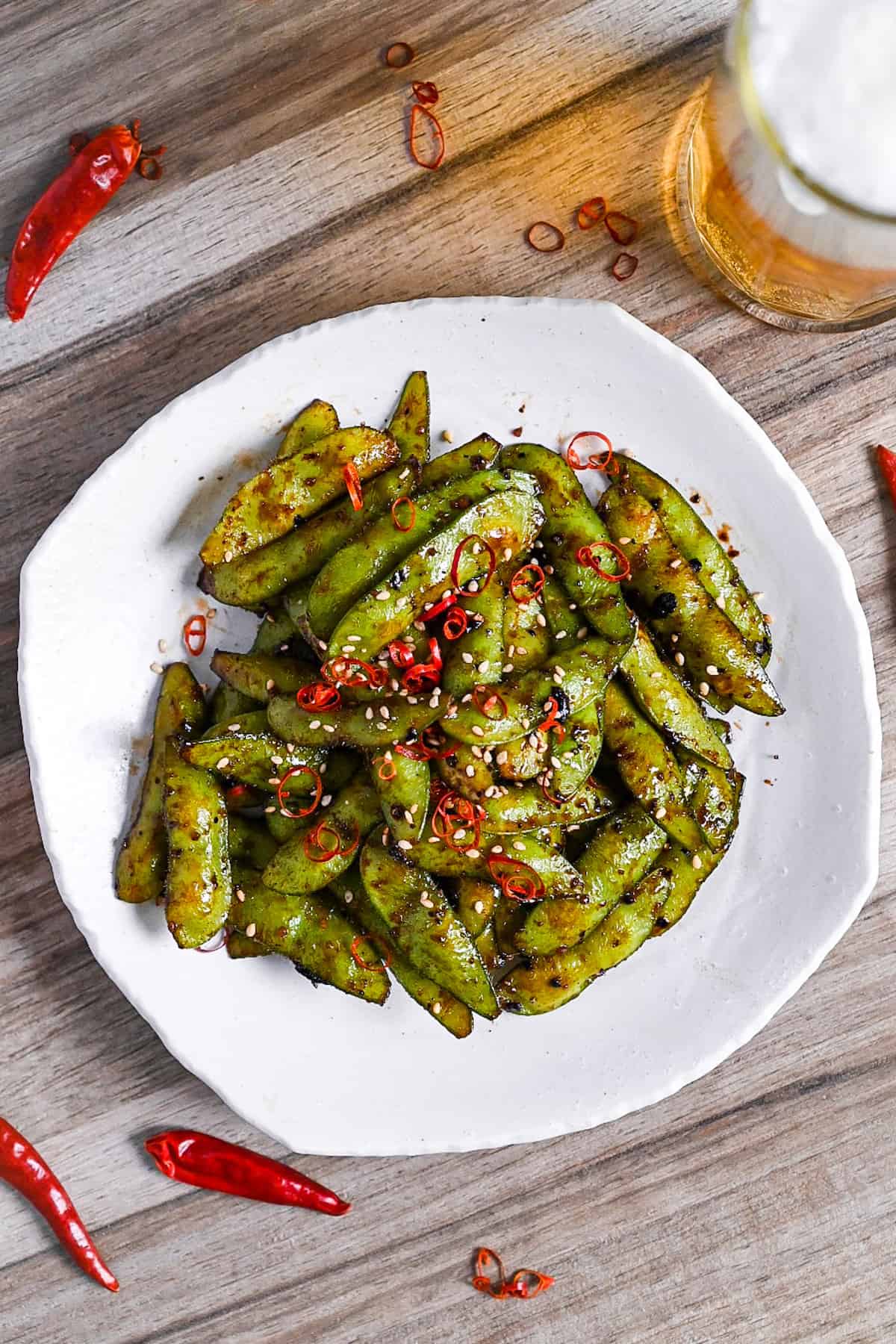 Stir fried edamame with garlic and oyster sauce glaze topped with dried chili and sesame seeds on a white plate