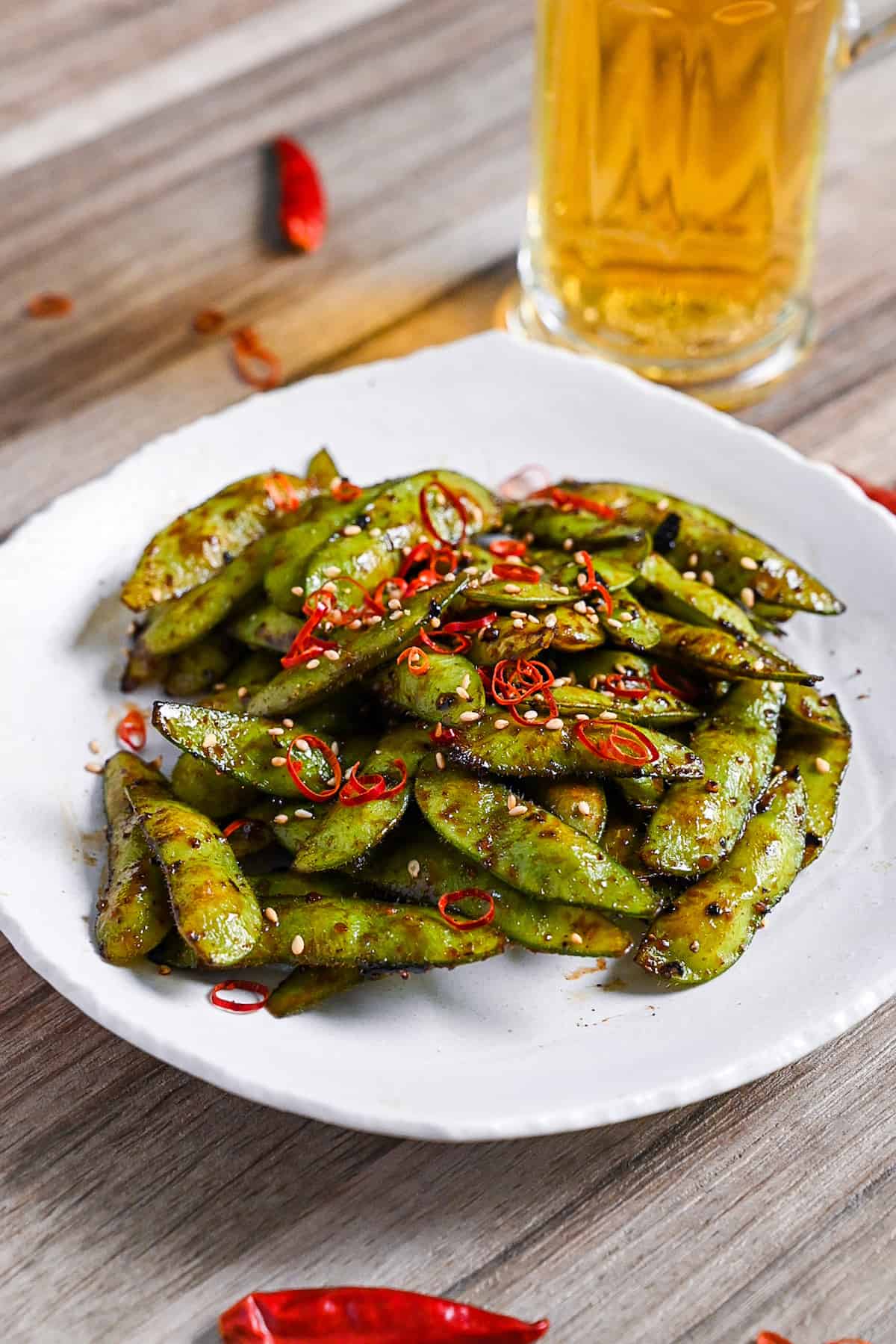 Stir fried edamame with garlic and oyster sauce glaze topped with dried chili and sesame seeds on a white plate