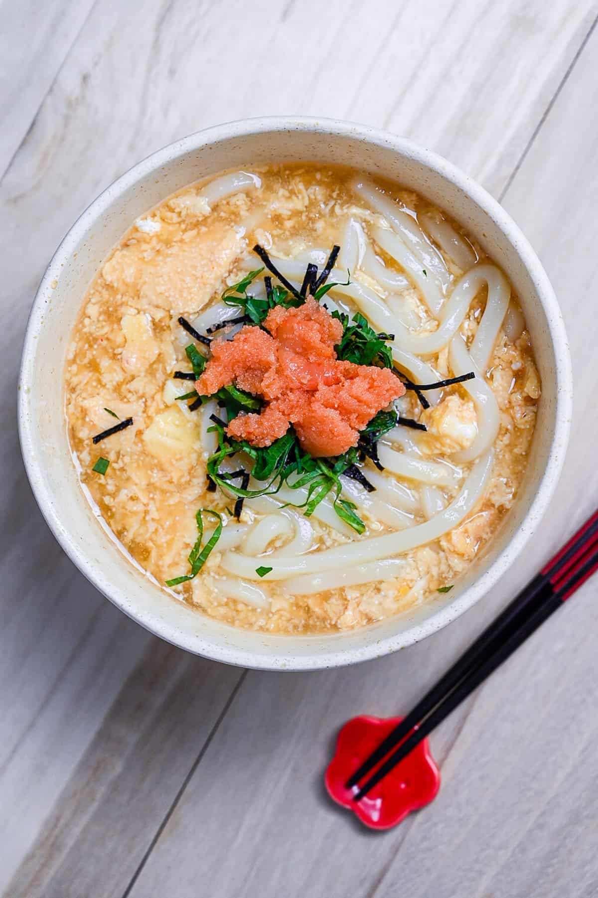 Mentaiko ankake udon served in a cream bowl and topped with shiso leaves. top down vertical