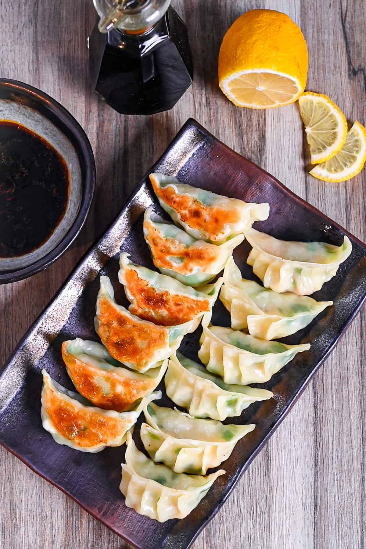 prawn gyoza arranged in rows on a brown rectangular plate with dipping sauce and lemon