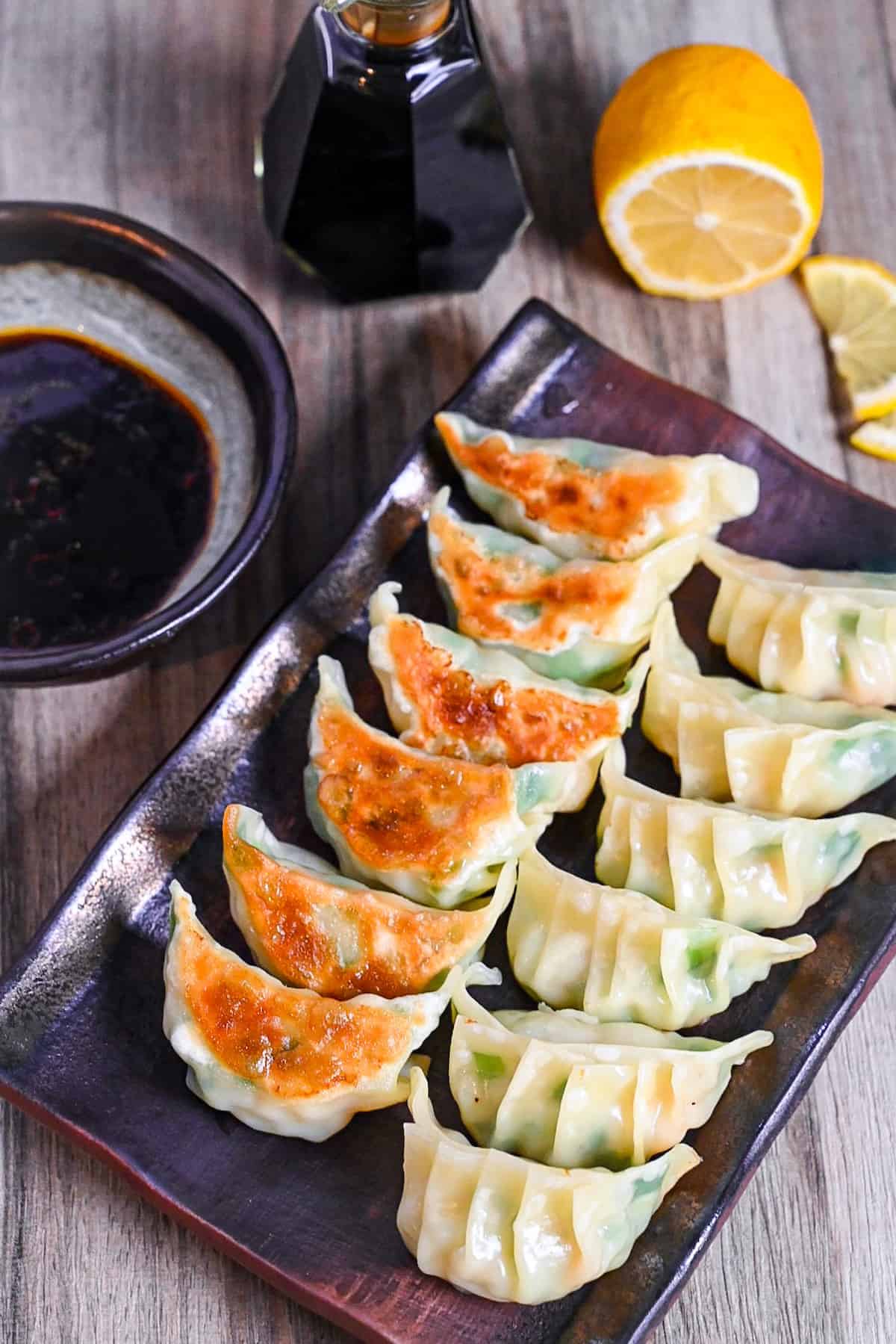 prawn gyoza arranged in rows on a brown rectangular plate with dipping sauce and lemon