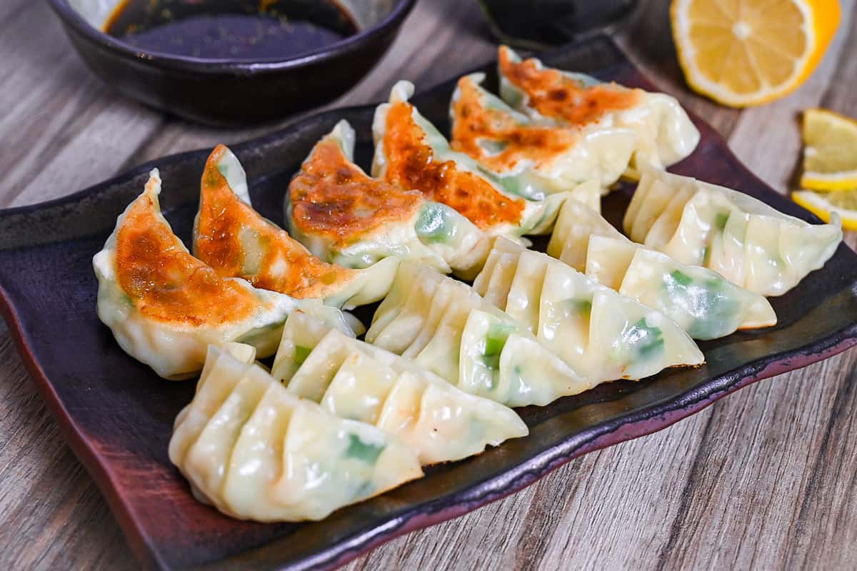 prawn gyoza arranged in rows on a brown rectangular plate with dipping sauce and lemon