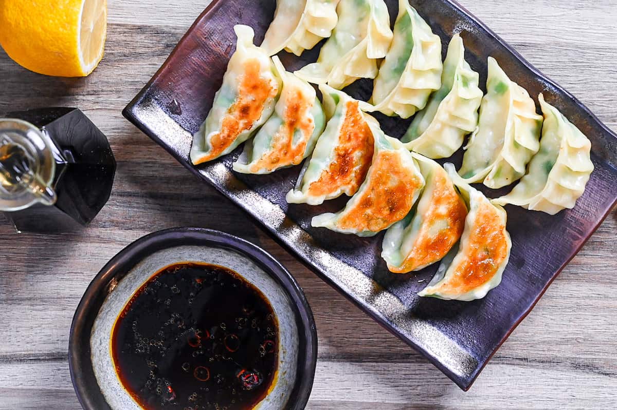 prawn gyoza arranged in rows on a brown rectangular plate with dipping sauce and lemon