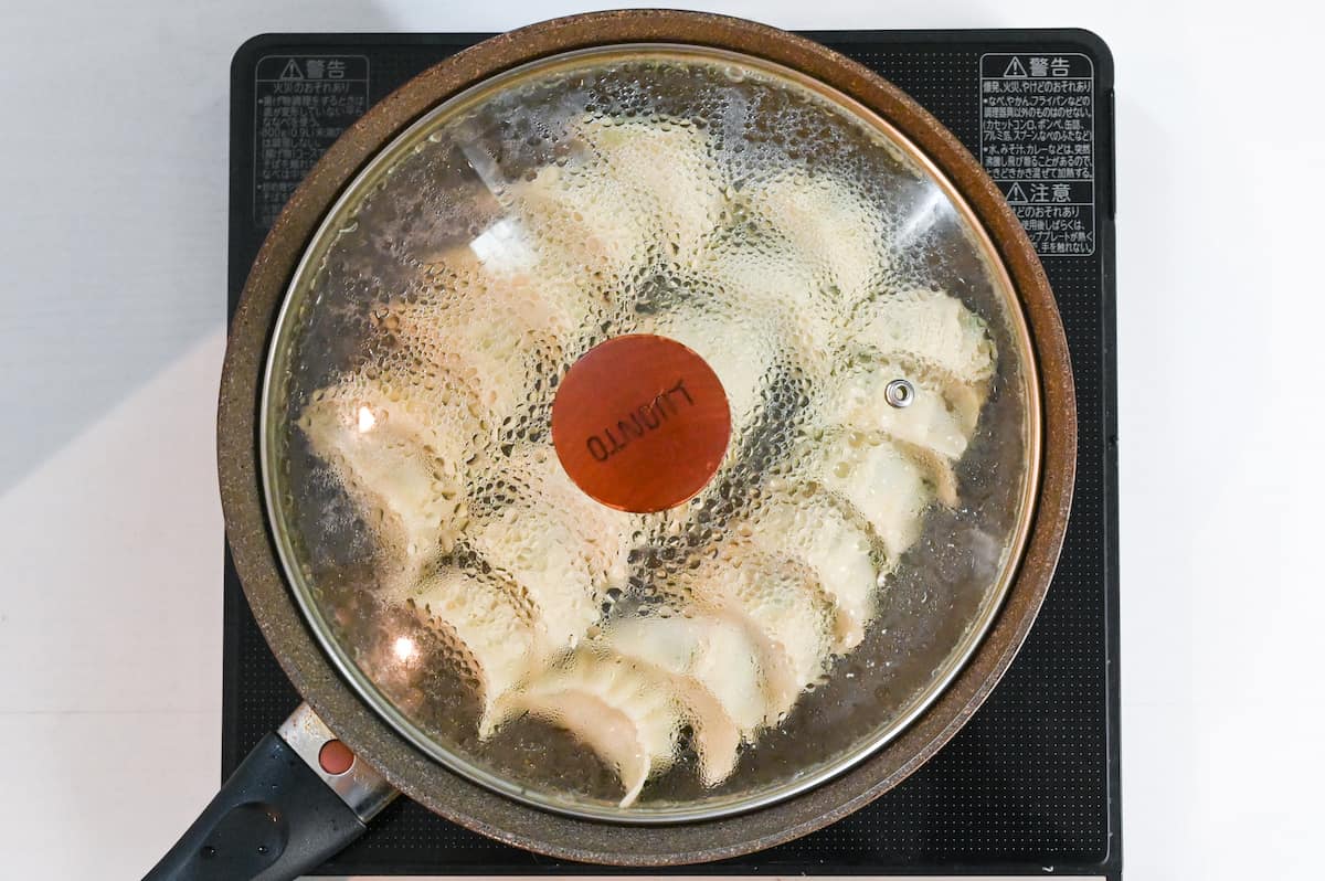 prawn gyoza steaming in a pan with lid