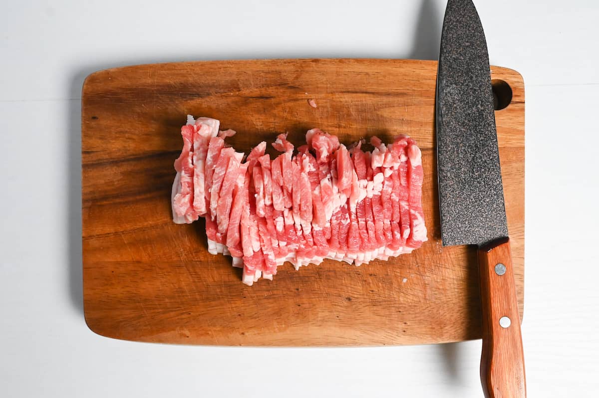 Thick slices of pork belly on a wooden chopping board with knife