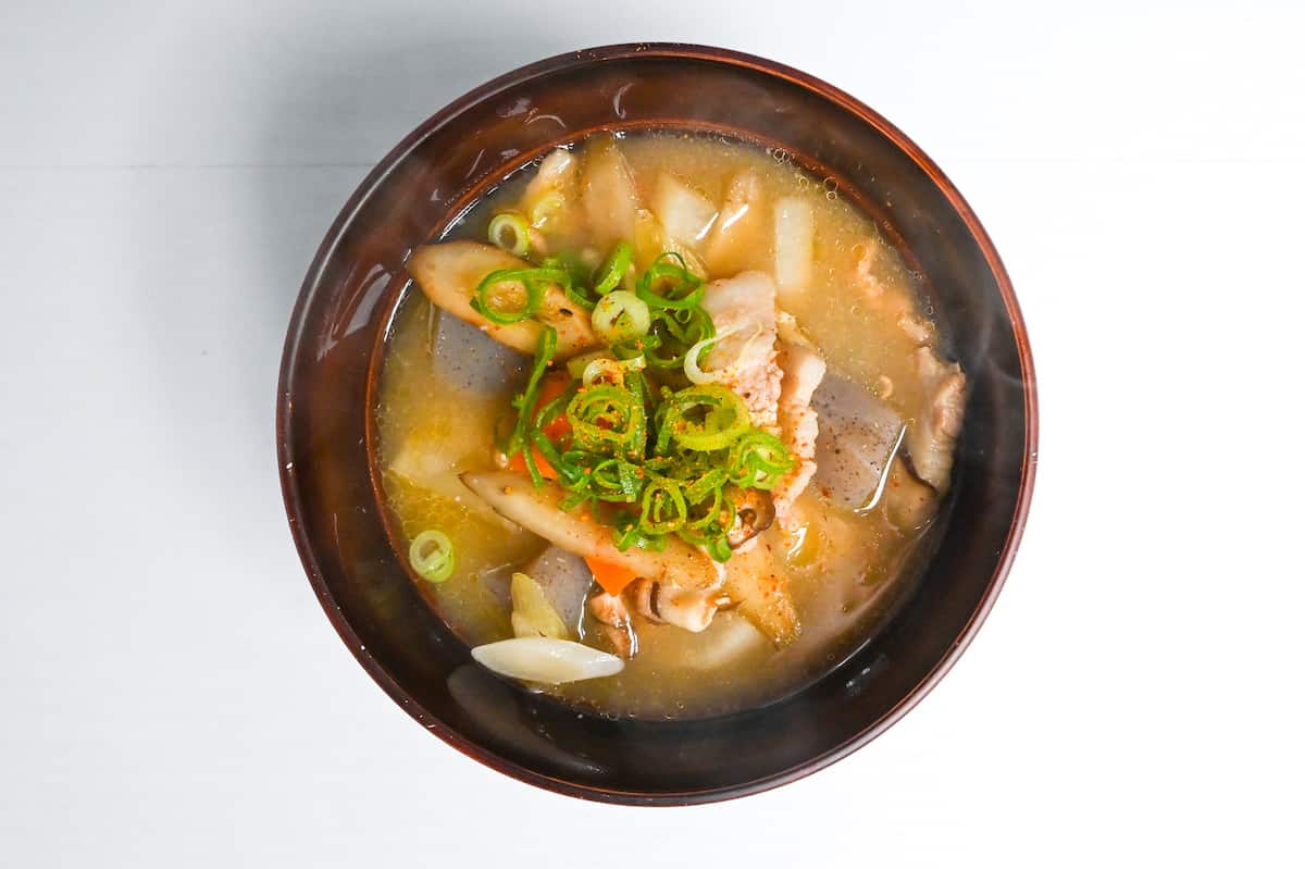 Tonjiru (pork miso soup) in a dark red bowl topped with chopped green onion and Japanese chili powder