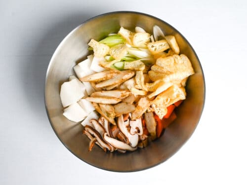 sliced fried tofu pouch, shiitake mushroom, daikon radish, green onion, carrot and burdock root in a metal bowl