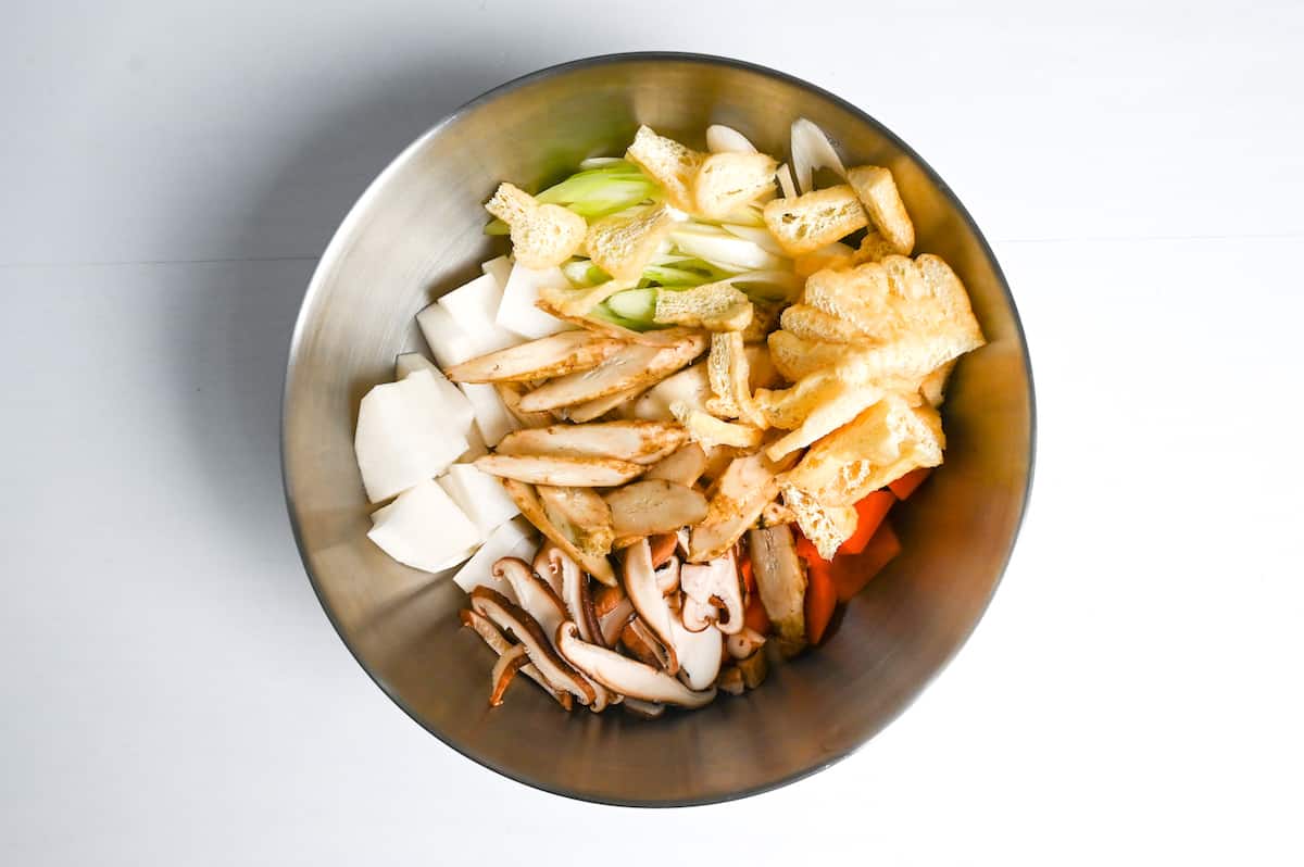 sliced fried tofu pouch, shiitake mushroom, daikon radish, green onion, carrot and burdock root in a metal bowl