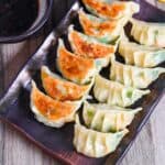 prawn gyoza arranged in rows on a brown rectangular plate with dipping sauce
