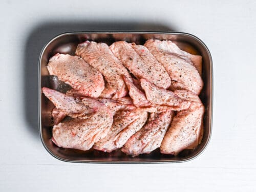 raw chicken wings seasoned with salt and pepper in a metal container