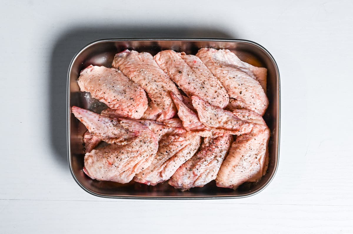 raw chicken wings seasoned with salt and pepper in a metal container